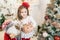 Adorable Caucasian girl wearing a festive outfit and holding a present surrounded by the winter holiday decor