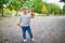 Adorable cheerful toddler girl with pigtails gathering yellow autumn leaves in park