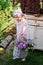 Adorable child girl in pink plaid dress near vintage bureau with lilacs in basket