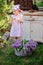 Adorable child girl in pink plaid dress with secateurs and basket of lilacs in spring garden