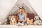 Adorable child sitting with corgi dogs in wigwam and writing