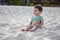 Adorable child in a swimsuit sits on a sandy beach in the sunshine