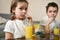 Adorable children drinking orange juice from straw sitting at the table at home