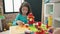 Adorable chinese girl playing with construction blocks sitting on table at kindergarten