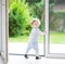 Adorable curly baby girl at big glass door to the garden