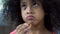 Adorable curly haired girl eating cookie at home, child snacking close-up