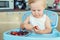 Adorable cute caucasian blond toddler boy enjoy tasting different seasonal fresh ripe organic berries sitting in highchair at home