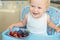 Adorable cute caucasian blond toddler boy enjoy tasting different seasonal fresh ripe organic berries sitting in highchair at home