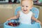 Adorable cute caucasian blond toddler boy enjoy tasting different seasonal fresh ripe organic berries sitting in highchair at home