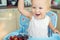 Adorable cute caucasian blond toddler boy enjoy tasting different seasonal fresh ripe organic berries sitting in highchair at home