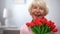 Adorable elderly female holding bunch of tulips and smiling at camera, present