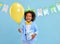 Adorable ethnic kid with birthday present and balloon in hands