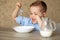 An adorable European baby eats porridge on his own. The boy does not like porridge. Plays with a spoon, pours milk. The child