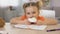 Adorable female child eating sweet cream cake sitting table, childhood happiness