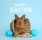 Adorable fluffy bunny in wicker basket and eggs on blue background. Happy Easter