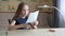 Adorable focused girl sitting at desk and cutting paper sheet