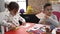 Adorable girl and boy sitting on table cutting paper at kindergarten