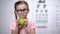 Adorable girl in glasses eating apple, natural vitamins for eyes, healthcare