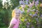 Adorable girl on spring blooming bush of lillac background in a park.