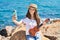 Adorable girl tourist make selfie by the smartphone playing ukulele at seaside