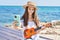 Adorable girl tourist make selfie by the smartphone playing ukulele at seaside