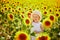 Adorable girl in white dress and straw hat in a field of sunflowers in Provence, France