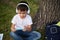 Adorable handsome elementary aged schoolboy with wireless headphones, fconcentrated on playing with smartphone, resting on the
