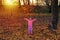 Adorable happy girl playing with fallen leaves in autumn park at sunset light.