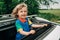 Adorable happy little boy stands in open car sunroof during trip at summer.