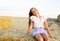 Adorable happy smiling ittle girl child sitting on a hay rolls in a wheat field