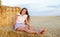 Adorable happy smiling ittle girl child sitting on a hay rolls in a wheat field