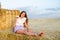 Adorable happy smiling ittle girl child sitting on a hay rolls in a wheat field