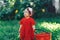 Adorable happy toddler girl with knitten flower crown wearing a red dress enjoying picnic in a beautiful blooming fruit garden