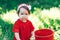 Adorable happy toddler girl with knitten flower crown wearing a red dress enjoying picnic in a beautiful blooming fruit garden