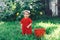 Adorable happy toddler girl with knitten flower crown wearing a red dress enjoying picnic in a beautiful blooming fruit garden