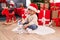 Adorable hispanic boy playing with robot toy sitting on floor by christmas tree at home