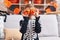 Adorable hispanic boy wearing skeleton costume holding pumpkin baskets over eyes at home