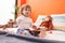 Adorable hispanic girl holding dolls sitting on bed at bedroom