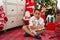 Adorable hispanic toddler writing on notebook sitting on floor by christmas tree at home