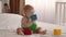 Adorable Infant Baby Sitting In Bed And Playing With Stacking Building Blocks