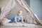 Adorable infant boy playing with toy tent in cozy blue playroom