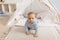 Adorable infant boy playing with toy tent in cozy blue playroom