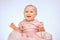 Adorable infant wearing a pink dress happily laughing while sitting on the floor.