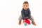 Adorable innocent biracial toddler boy in warm clothes sitting on a red skateboard. Studio show over white background.
