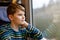 Adorable kid boy traveling by train. Happy smiling child looking out of the window during train moving. Kid dreaming and