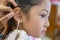 Adorable little Asian girl having ear piercing process.