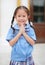 Adorable little Asian girl in school uniform is pay respect Wai Thai Greetings
