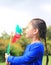 Adorable little Asian kid girl blowing wind turbine in the summer garden