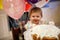 Adorable little baby girl celebrating first birthday. Baby eating marshmellows decoration on homemade cake, indoor.