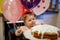 Adorable little baby girl celebrating first birthday. Baby eating marshmellows decoration on homemade cake, indoor.